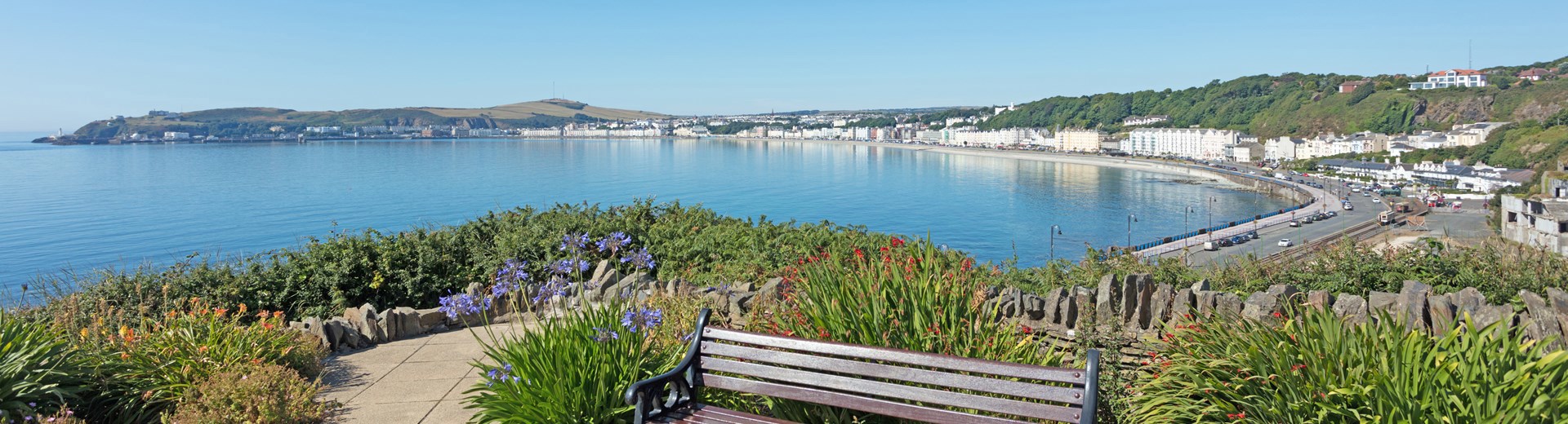A bench sat on a hill in Douglas bay, Isle Of Man. The sky is blue. 